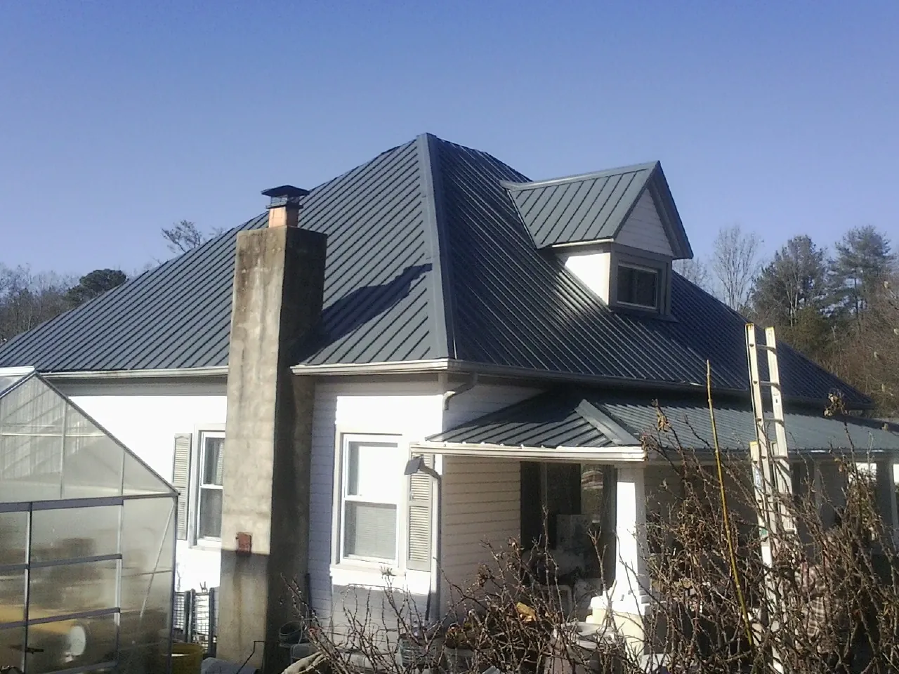 Dark blue standing seam metal roof on a white farmhouse with dormer — Slate & Tile Roof Repair by Roofing Brothers in Bixby