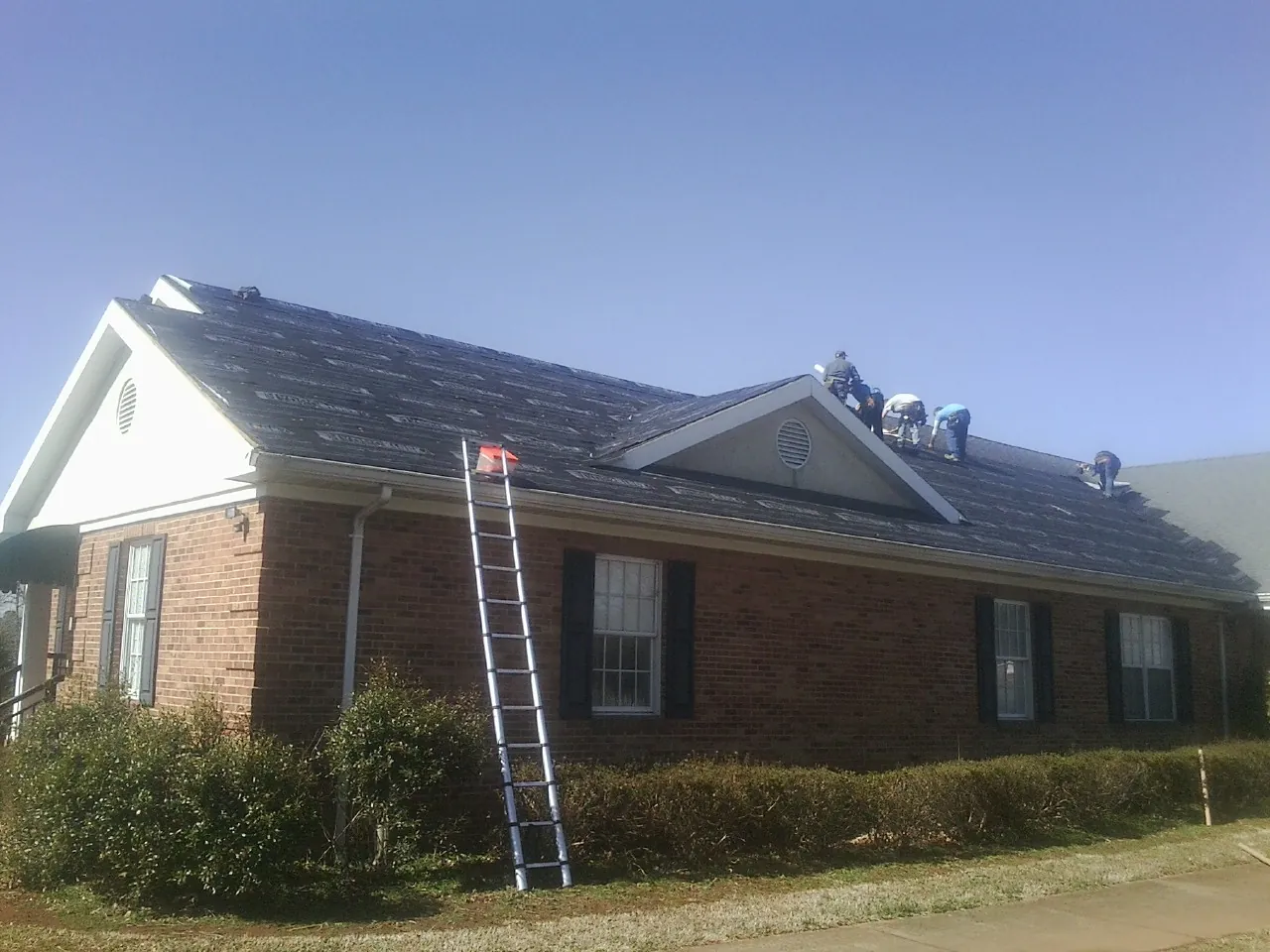 Crew tearing shingles off a brick ranch roof with a ladder set — Metal Roof Repair work by our crew in Bixby