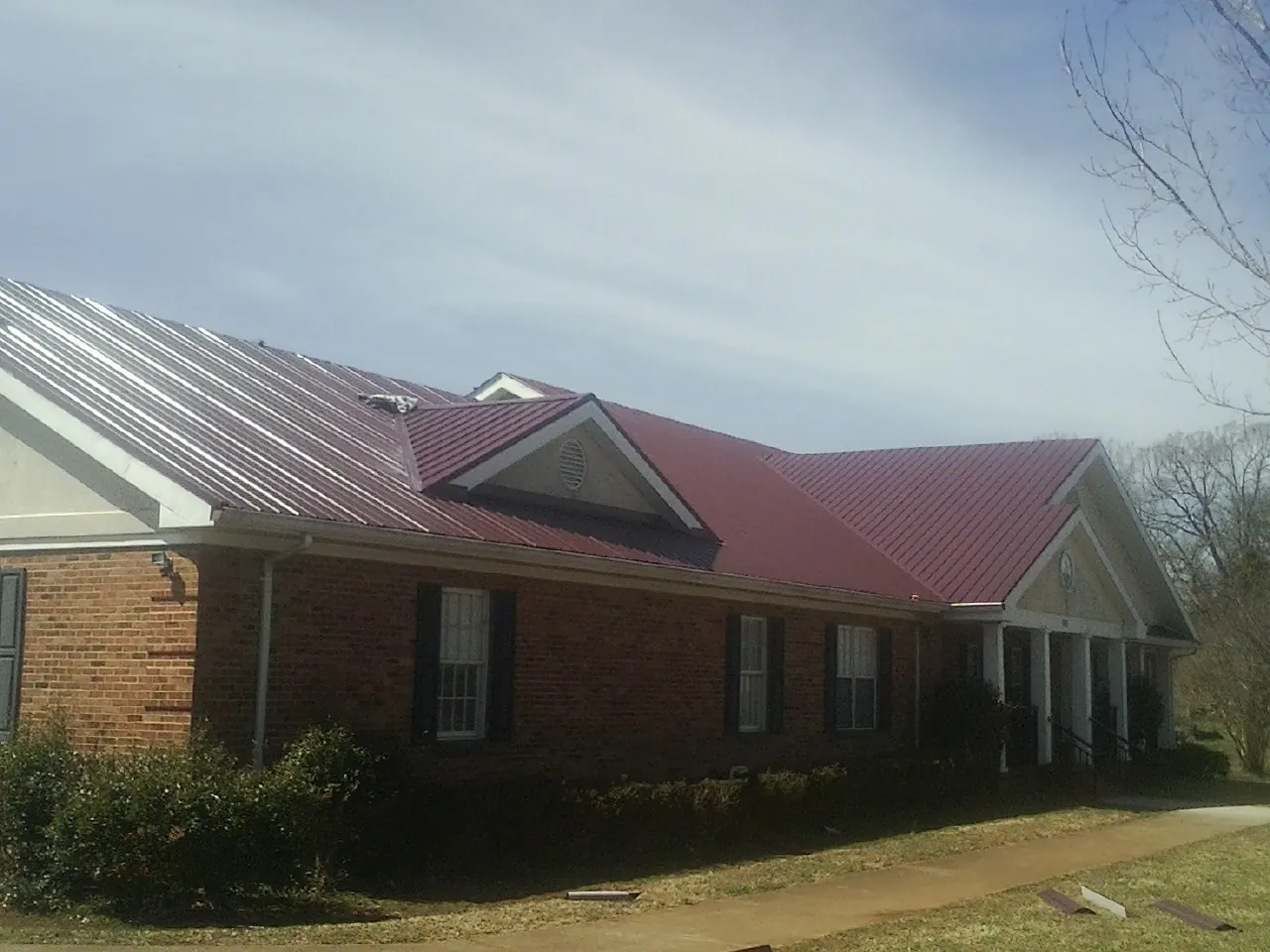 Red metal roof with gabled entries on a long brick building, from a Hail Damage Roof Repair job in Bixby