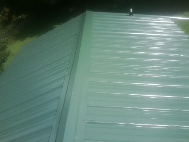 New green metal panels meeting at the ridge of a roof — Flat Roof Repair work by our crew in Bixby