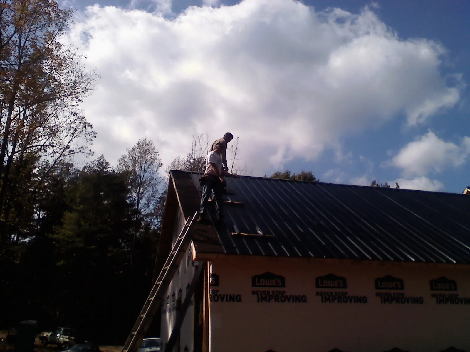 Roofer fastening dark metal panels high against a cloudy sky, from a Roof Inspection job in Bixby