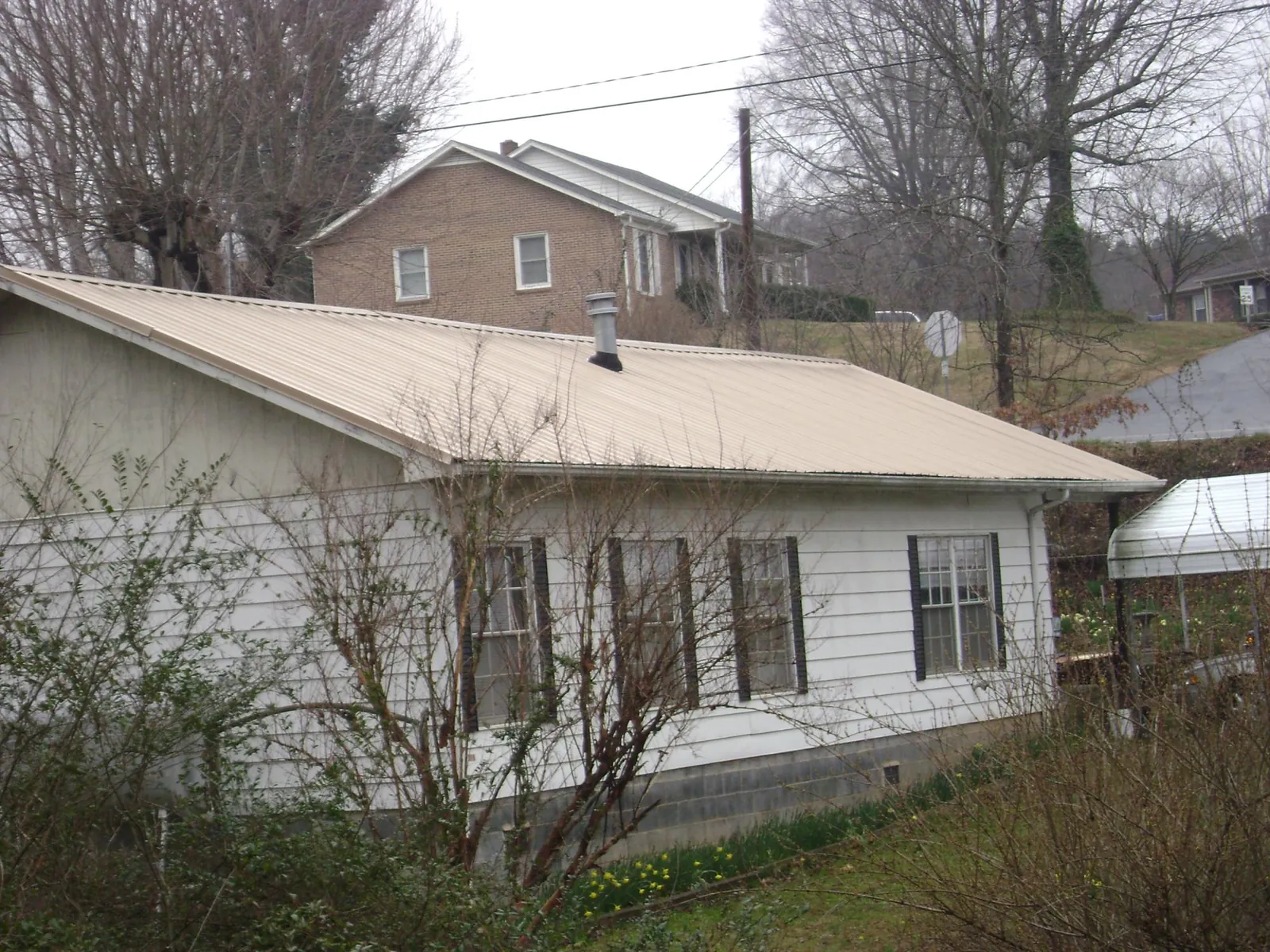 Tan metal roof on a white sided house set into a hillside — Commercial Roofing by Roofing Brothers in Bixby